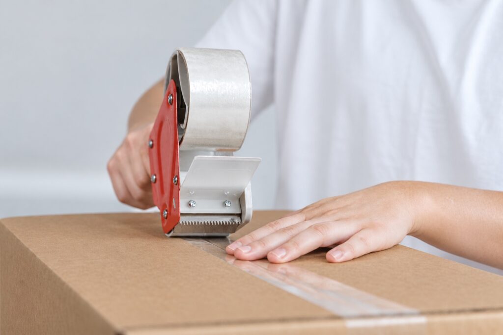 Hands sealing a corrugated shipping carton with a tape dispenser